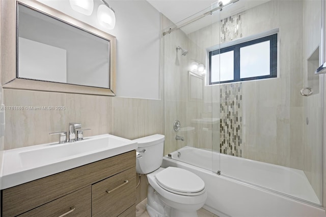 bathroom with bath / shower combo with glass door, vanity, tile walls, and toilet