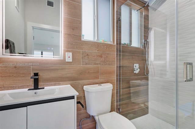 full bath with visible vents, a shower stall, tile walls, toilet, and vanity