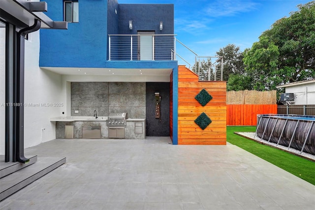 view of patio with a sink, fence, grilling area, exterior kitchen, and a balcony