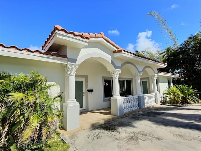 view of front of house featuring stucco siding, a porch, and a tile roof