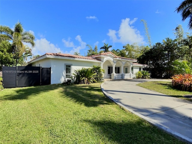 mediterranean / spanish-style home featuring stucco siding, a tile roof, a front lawn, and fence