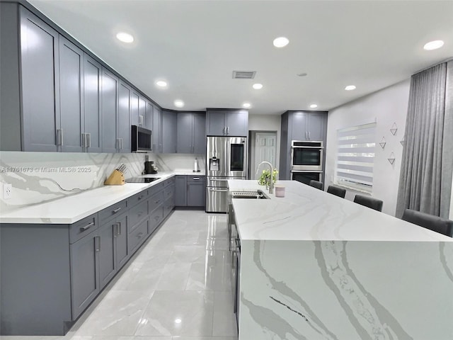 kitchen with visible vents, gray cabinets, a sink, light stone counters, and appliances with stainless steel finishes