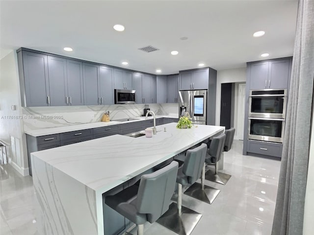 kitchen featuring gray cabinetry, light stone countertops, a breakfast bar, stainless steel appliances, and a sink