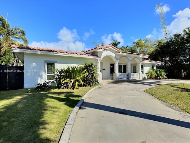 mediterranean / spanish-style house featuring a tiled roof, a porch, concrete driveway, a front yard, and stucco siding