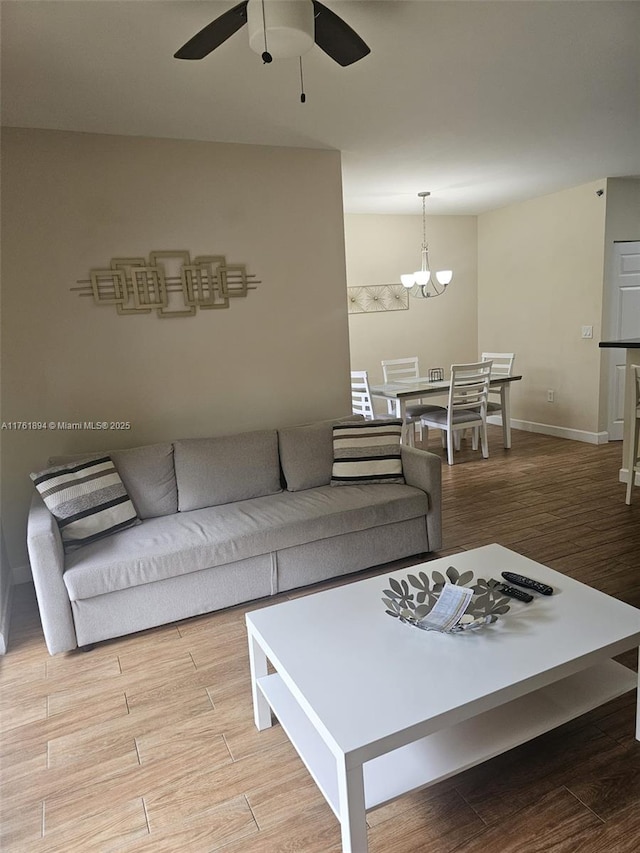 living area featuring baseboards, wood finished floors, and ceiling fan with notable chandelier