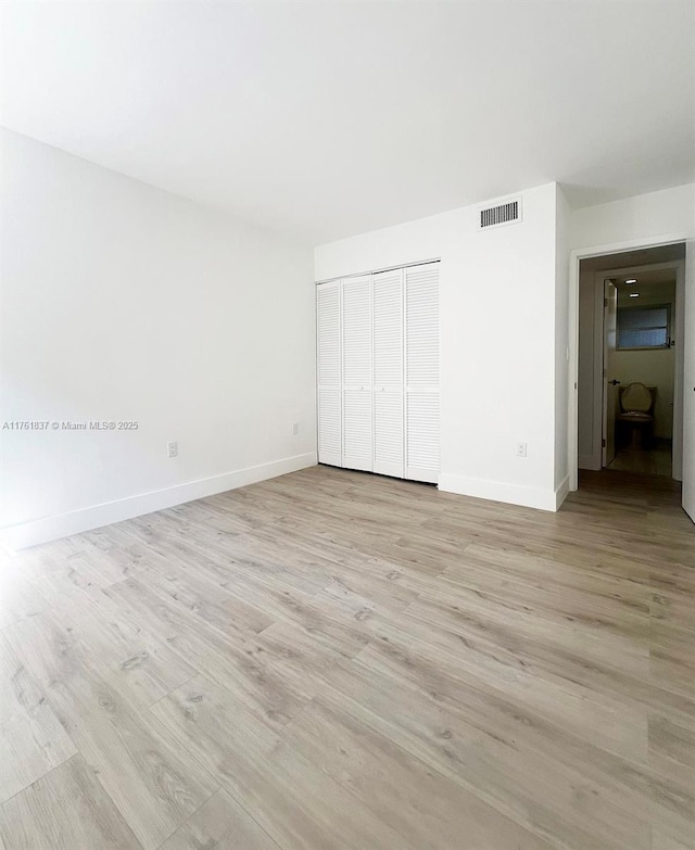 unfurnished bedroom with light wood-style flooring, baseboards, visible vents, and a closet