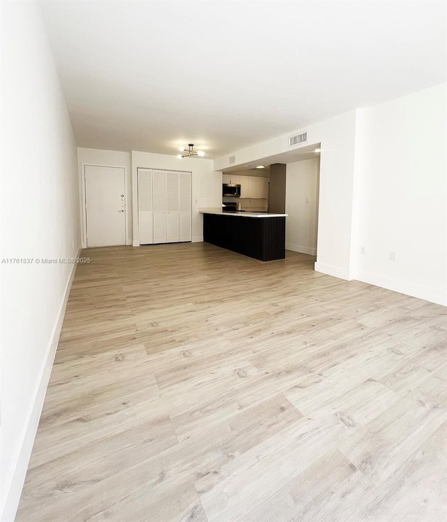 unfurnished living room with visible vents, light wood-type flooring, and baseboards