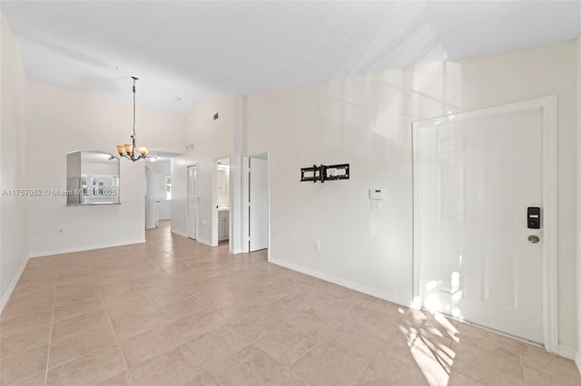 unfurnished living room with a notable chandelier, lofted ceiling, arched walkways, light tile patterned floors, and baseboards