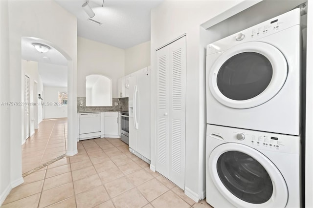 laundry room with baseboards, visible vents, laundry area, light tile patterned flooring, and stacked washer / dryer