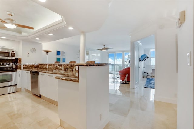 kitchen with a ceiling fan, a peninsula, a sink, stainless steel appliances, and white cabinets