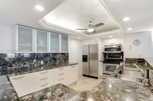 kitchen featuring dark stone counters, a sink, stainless steel appliances, white cabinetry, and a raised ceiling