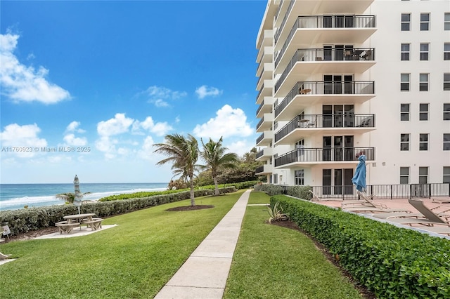 view of property's community featuring a water view, a lawn, and a beach view