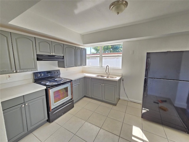 kitchen featuring stainless steel electric range, freestanding refrigerator, a sink, gray cabinetry, and under cabinet range hood