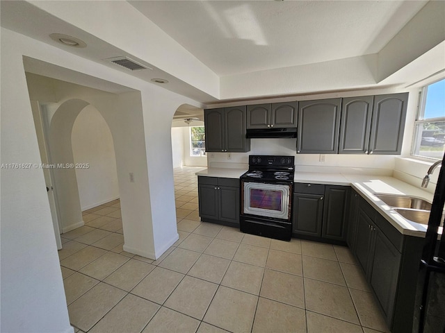 kitchen featuring under cabinet range hood, light tile patterned floors, range with electric stovetop, and a sink