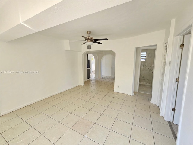 spare room featuring arched walkways, light tile patterned floors, baseboards, and a ceiling fan