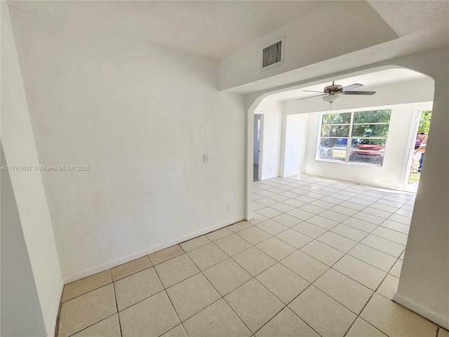 empty room featuring visible vents, ceiling fan, baseboards, light tile patterned floors, and arched walkways