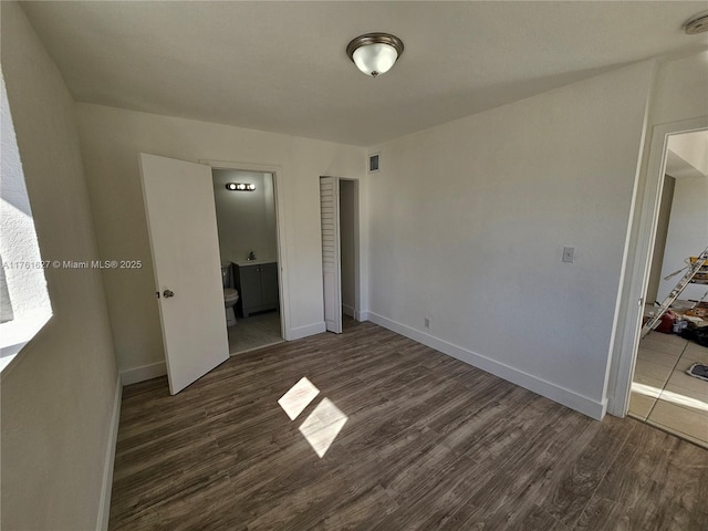 unfurnished bedroom with connected bathroom, wood finished floors, visible vents, and baseboards