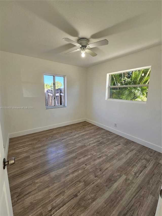 unfurnished room with baseboards, plenty of natural light, ceiling fan, and dark wood-style flooring