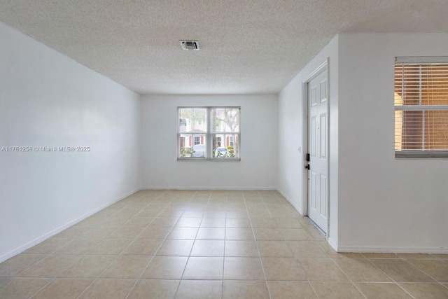 spare room featuring tile patterned floors, visible vents, a textured ceiling, and baseboards