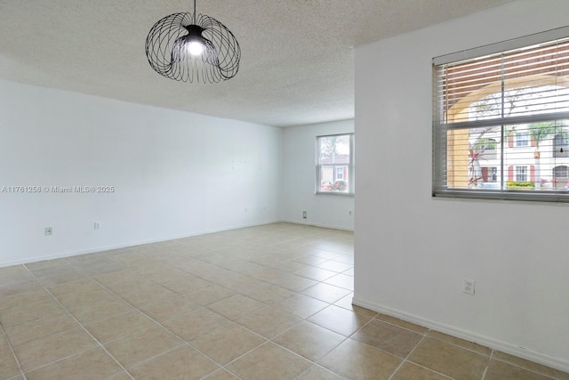 spare room featuring light tile patterned flooring, a textured ceiling, and baseboards