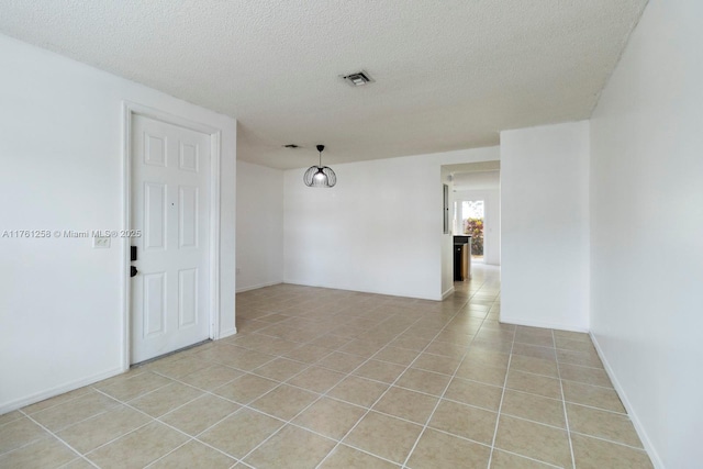 empty room featuring light tile patterned flooring, baseboards, visible vents, and a textured ceiling