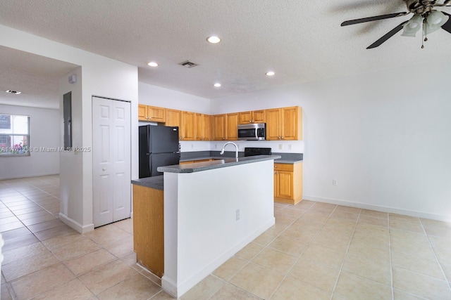 kitchen with dark countertops, a center island with sink, recessed lighting, freestanding refrigerator, and stainless steel microwave