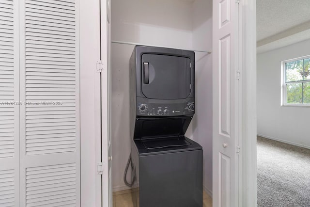 laundry area with stacked washer and clothes dryer, a textured ceiling, carpet floors, baseboards, and laundry area