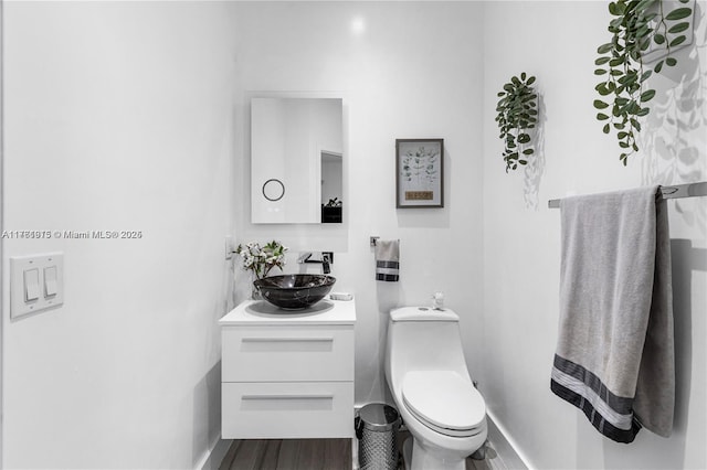 bathroom with baseboards, toilet, wood finished floors, and vanity