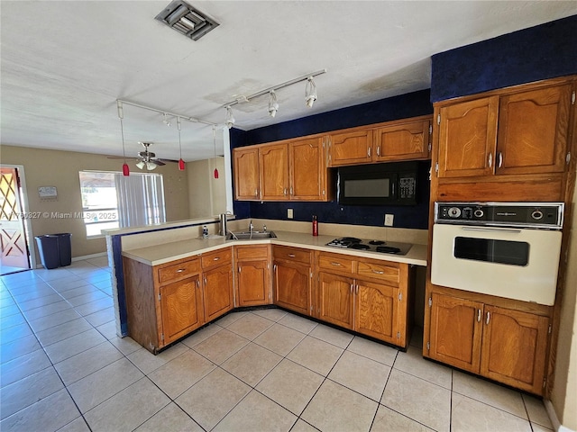 kitchen with visible vents, light tile patterned floors, a peninsula, brown cabinetry, and black appliances