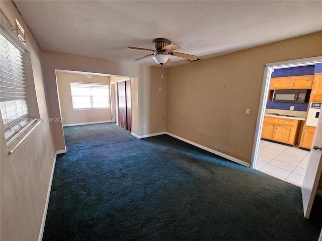 empty room with light tile patterned floors, a ceiling fan, baseboards, and light carpet