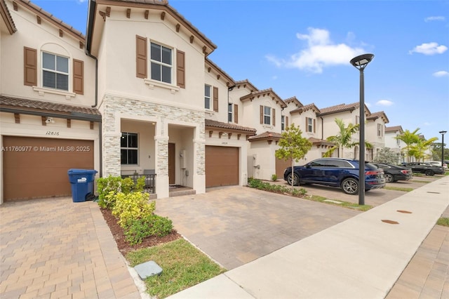 mediterranean / spanish-style house with an attached garage, stucco siding, a tiled roof, decorative driveway, and a residential view