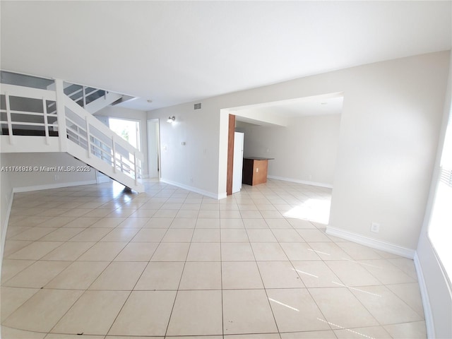 unfurnished living room featuring stairway, baseboards, and light tile patterned flooring