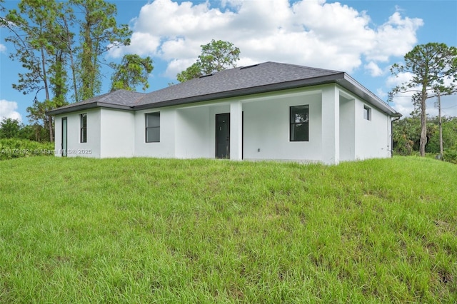 back of property featuring a lawn, roof with shingles, and stucco siding