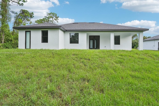 back of property with a lawn, roof with shingles, and stucco siding