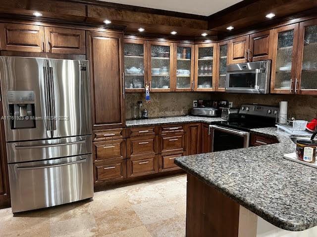 kitchen with dark stone counters, glass insert cabinets, a peninsula, and stainless steel appliances