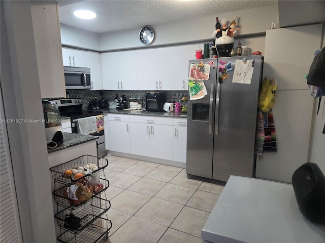 kitchen with light tile patterned floors, stainless steel appliances, white cabinets, dark countertops, and backsplash