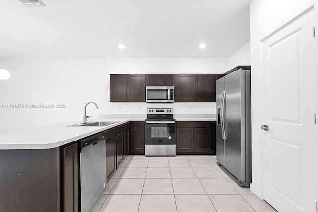 kitchen with dark brown cabinets, light countertops, light tile patterned floors, stainless steel appliances, and a sink