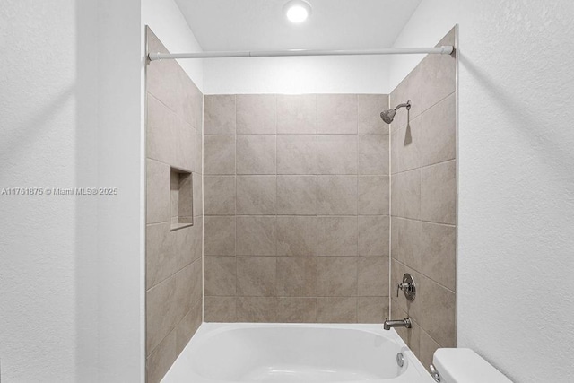 bathroom featuring tub / shower combination, toilet, and a textured wall