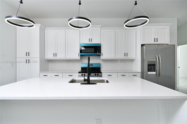 kitchen with a center island with sink, appliances with stainless steel finishes, hanging light fixtures, white cabinets, and a sink