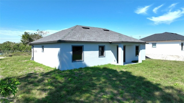 back of property with a yard, roof with shingles, and stucco siding