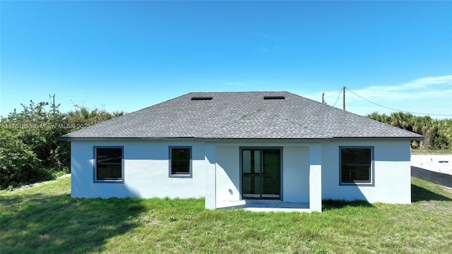 rear view of property with a yard, stucco siding, and a shingled roof