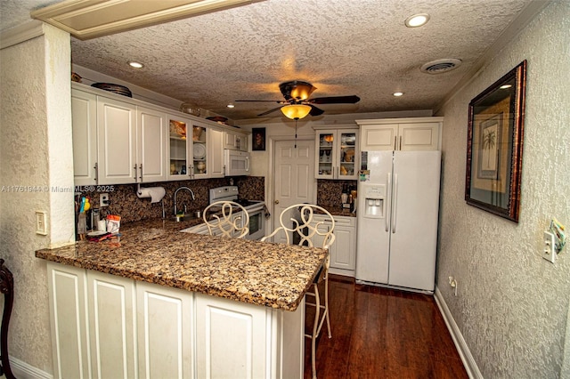 kitchen with visible vents, a peninsula, a textured wall, white appliances, and dark wood-style flooring