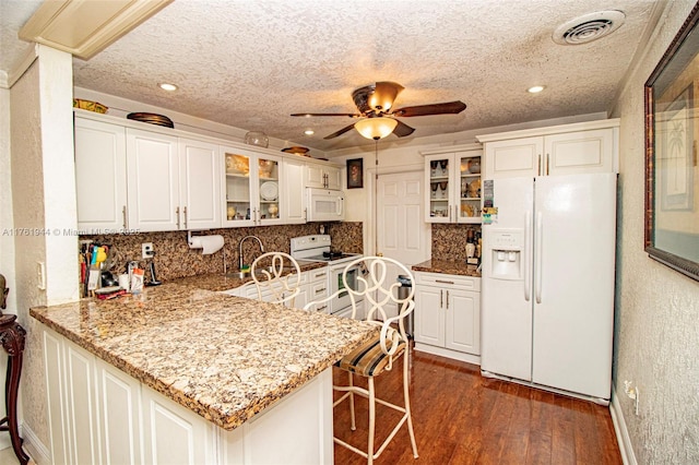 kitchen featuring white appliances, visible vents, a peninsula, dark wood-style flooring, and glass insert cabinets