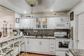 kitchen with a sink, white appliances, backsplash, and white cabinetry