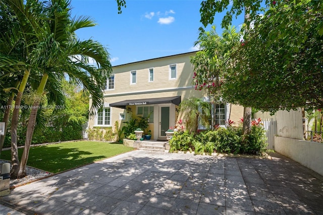 rear view of house featuring a lawn and stucco siding