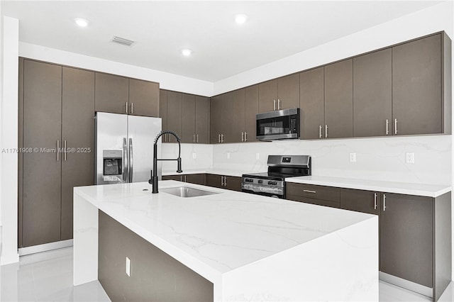 kitchen featuring visible vents, light stone countertops, stainless steel appliances, and a sink