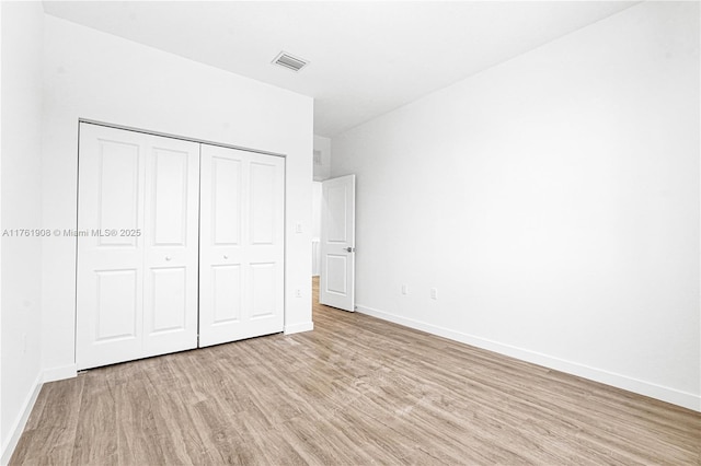 unfurnished bedroom with a closet, baseboards, visible vents, and light wood finished floors