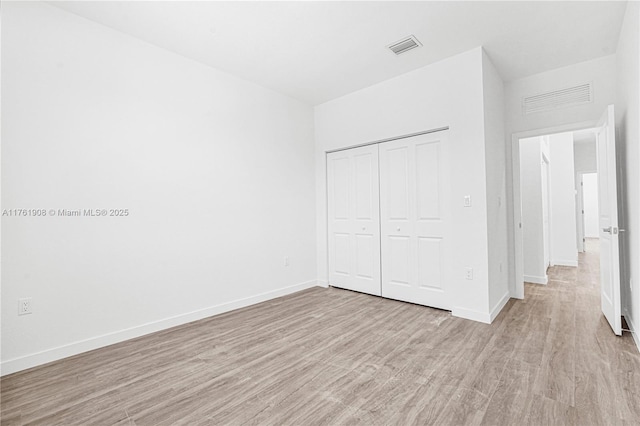 unfurnished bedroom featuring light wood-style floors, visible vents, a closet, and baseboards