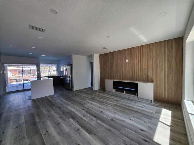 unfurnished living room with visible vents, wood walls, a fireplace, wood finished floors, and a textured ceiling