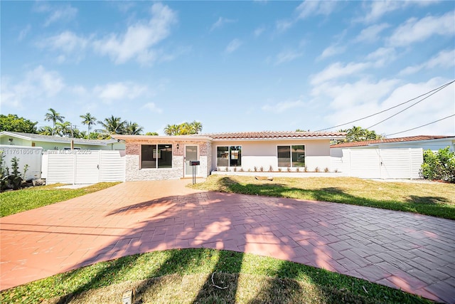 ranch-style home featuring a patio, a tile roof, a front yard, and a gate